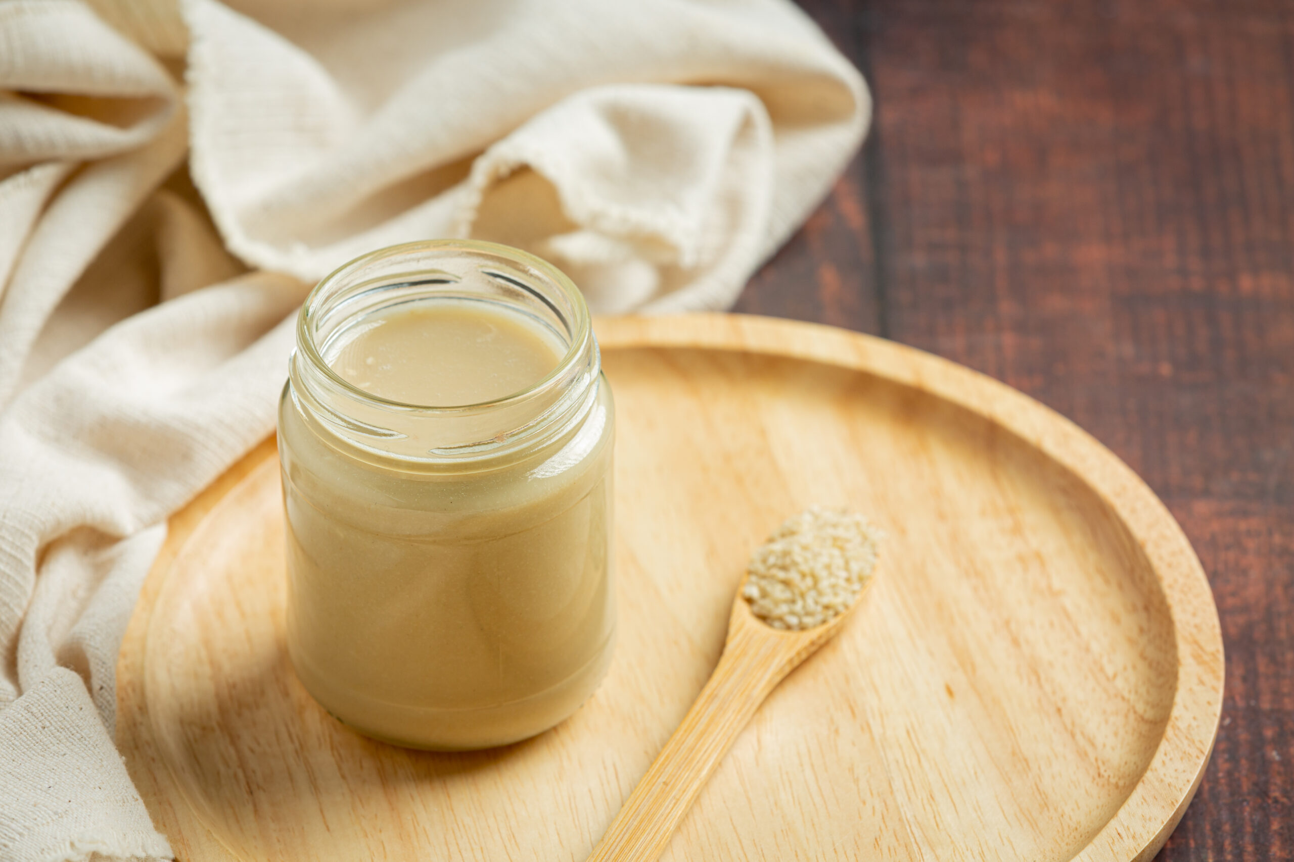 tahini and sesame seeds on dark wooden background